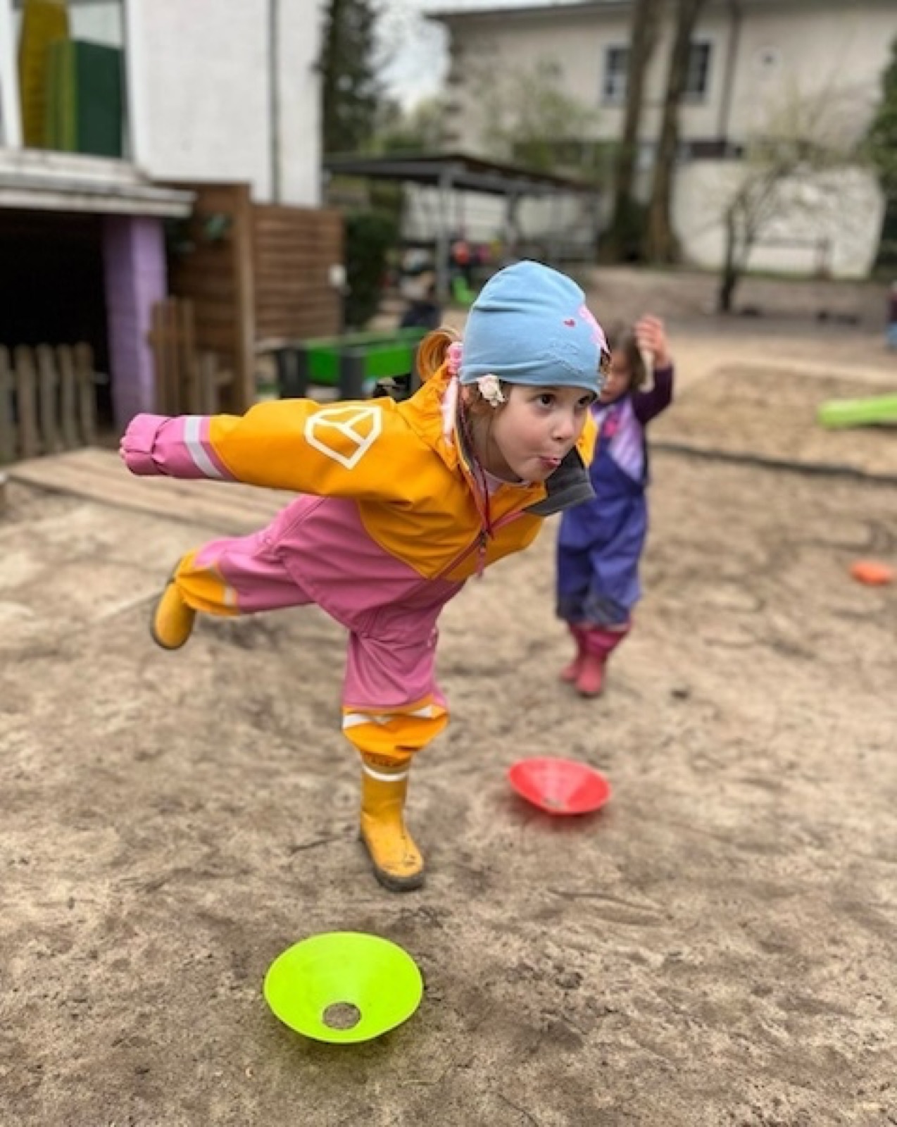 A girl in a snowsuit balances on one leg