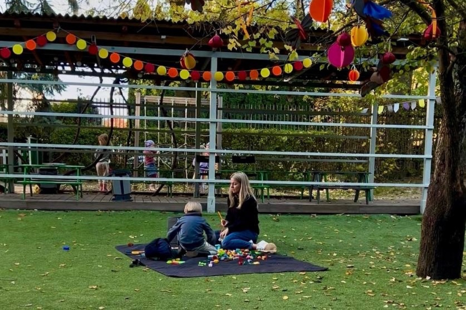 A teacher plays with a child on a blanket in the garden
